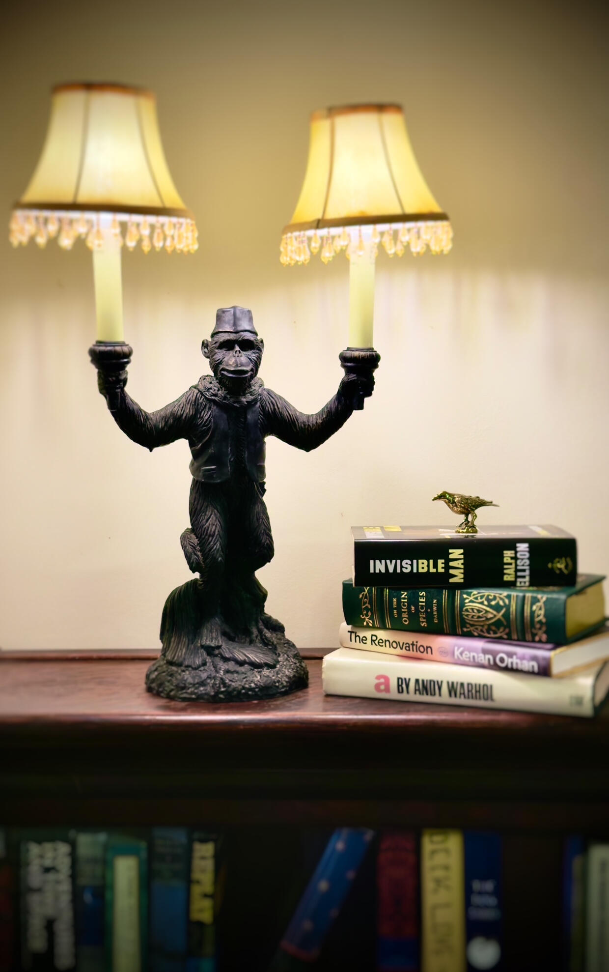 ByrdHaus Monkey Lamp Vintage monkey figurine holding two fringed table lamps, standing by a stack of books on the top of a barrister bookcase.
